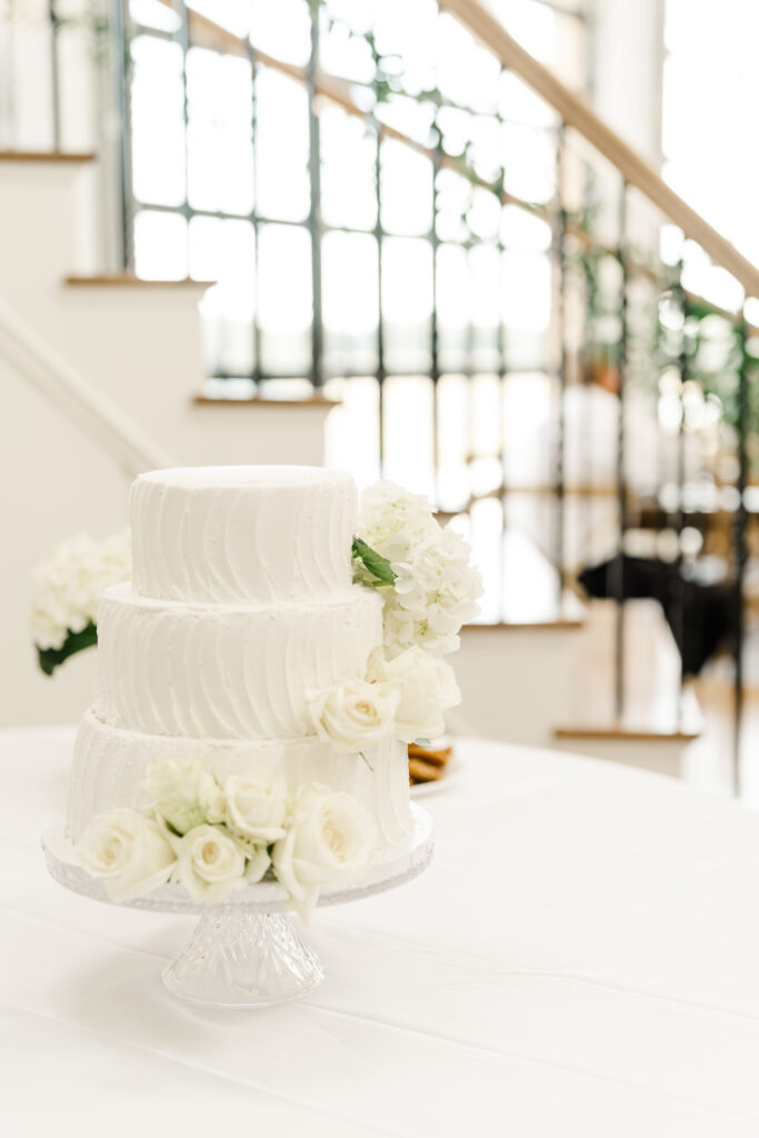 white wedding cake with white roses and hydrangeas inside a wedding venue dallas texas in front of a staircase 