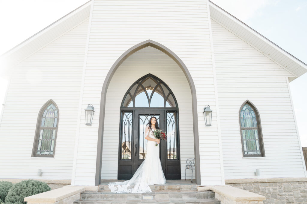 bride in front of lubbock wedding venue holding a bouquet of red roses