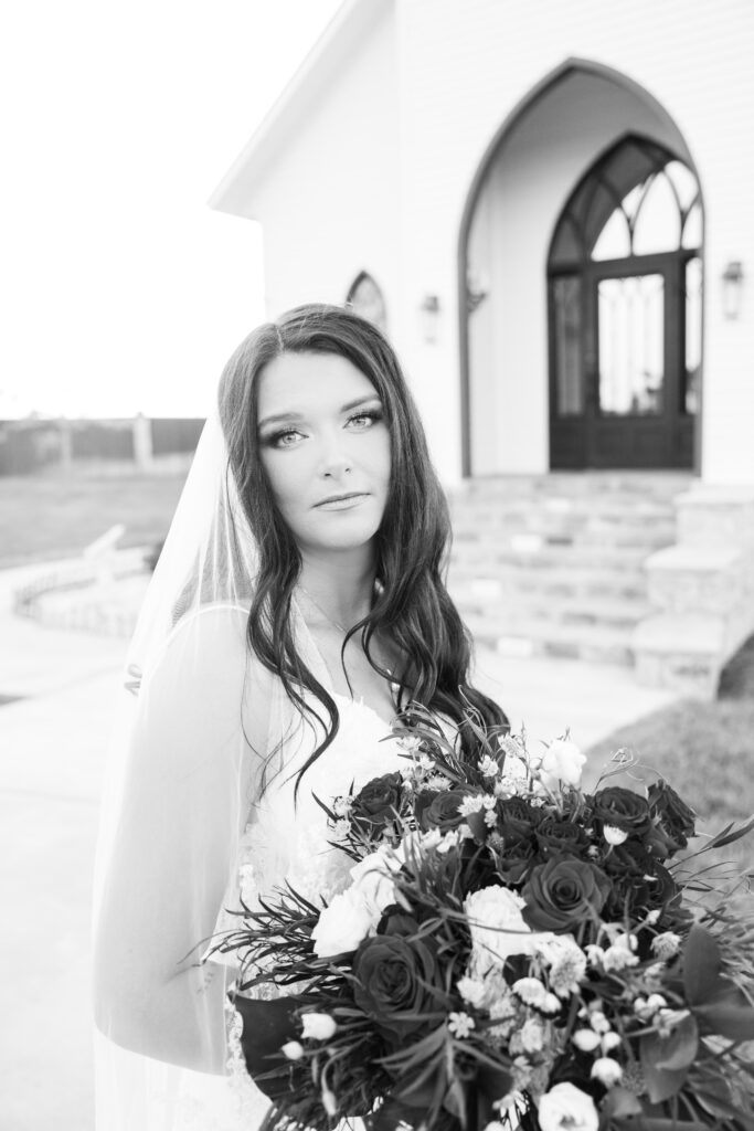 black and white photo of bride in front of a chapel 